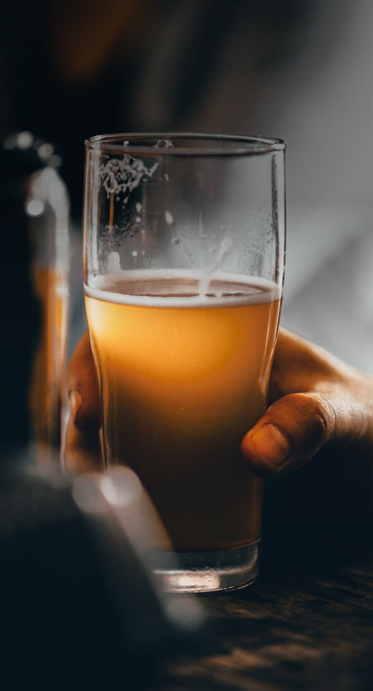 Hand holding a half-full beer glass on a bar in a dark room
